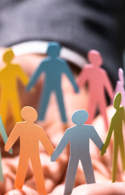 A group of colourful people figures made out of paper holding hands in a circle placed on a man's hands 