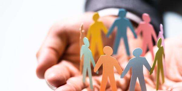 A group of colourful people figures made out of paper holding hands in a circle placed on a man's hands 