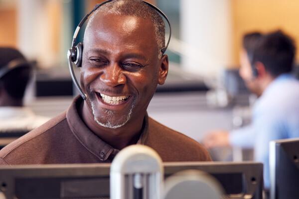 A black man with headphones on smiling in front of a computer monitor