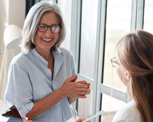 A white older woman and a younger woman with glasses having a conversation by the window