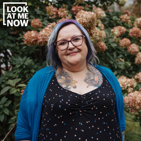 A white woman with tattoos on her chest standing in front of a flowering tree