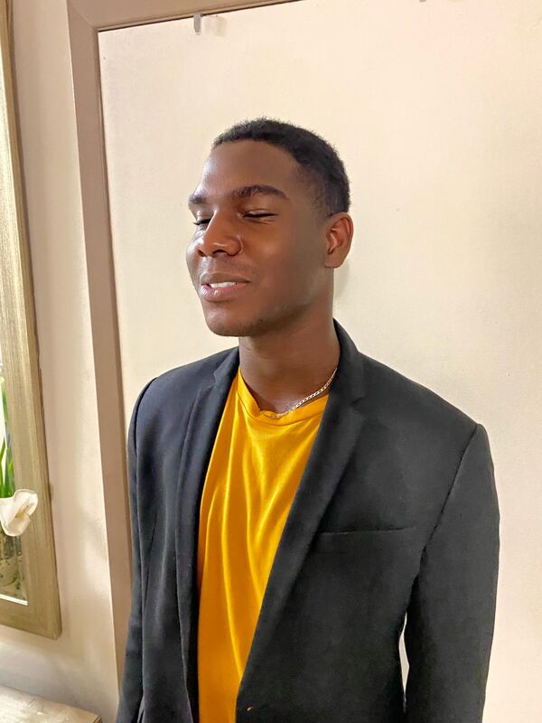 Photo de Michel-Antony, un jeune homme noir au cheveux courts portant un chandail jaune et un veston gris foncé.