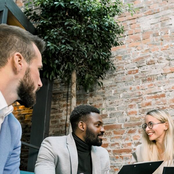A black man and two white people in suits having a conversation holding laptops 